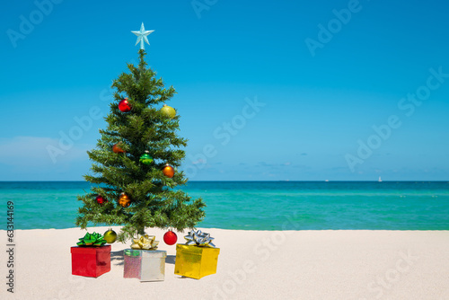 Christmas Tree on the beach. Merry Christmas. Present gift box. Happy New Year. Winter Holidays. Miami Florida vacation. Decorated Christmas pine or fir tree. Tropical Nature. Blue ocean on background © artiom.photo
