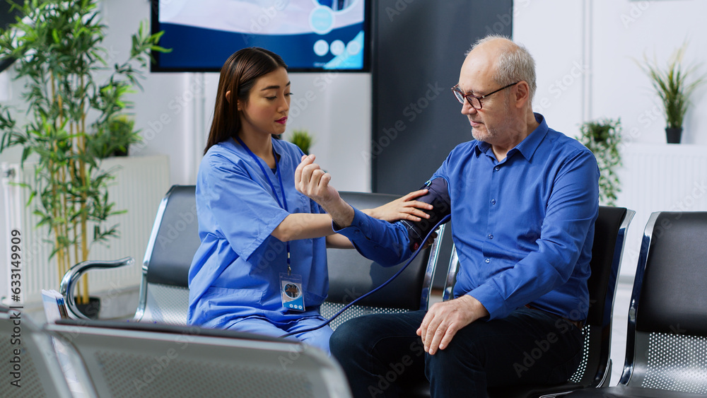 Obraz premium Assistant measuring old man hypertension using medical tonometer during checkup visit consultation in hospital waiting area. Nurse examining elderly patient blood pressure in reception