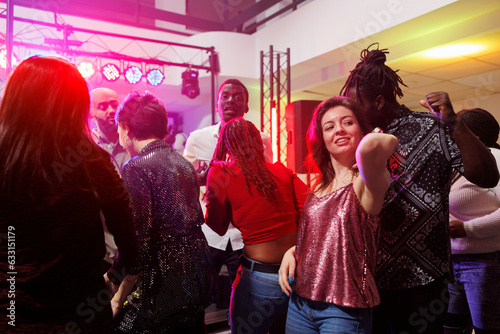 Multiracial couple dancing together while partying in crowded nightclub. Man and woman clubbing and having fun on dancefloor illuminated with spotlights at club discotheque