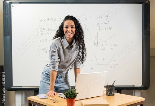 Portrait of young Mixed Race female teacher looking at camera. Happy adult lecturer at classroom standing after giving lecture. Satisfied high school teacher smiling while his students studying.