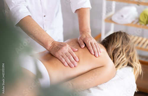 Hands of old masseur conducting back massage for woman client in procedure room