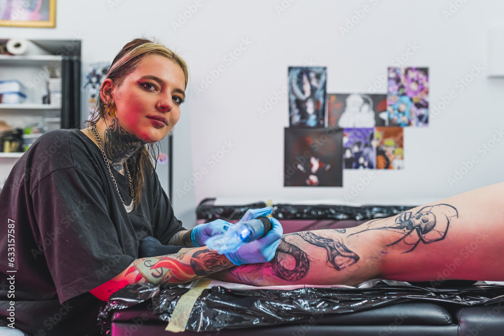 Tattooed caucasian female artist during the process of tattooing her client. Protective gloves and profesional equipment. . High quality photo