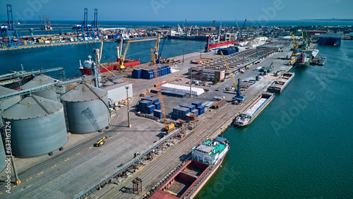 Loading grain into holds of sea cargo vessel in seaport from silos of grain storage. Bunkering of dry cargo ship with grain. Aerial top view