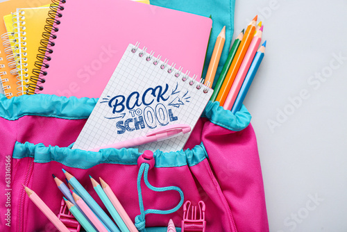 Notebook with text BACK TO SCHOOL, backpack and stationery on light background