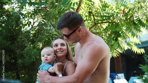 Family of three on simmer vacation. Topless man wearing glasses embraces his wife holding a child. photo