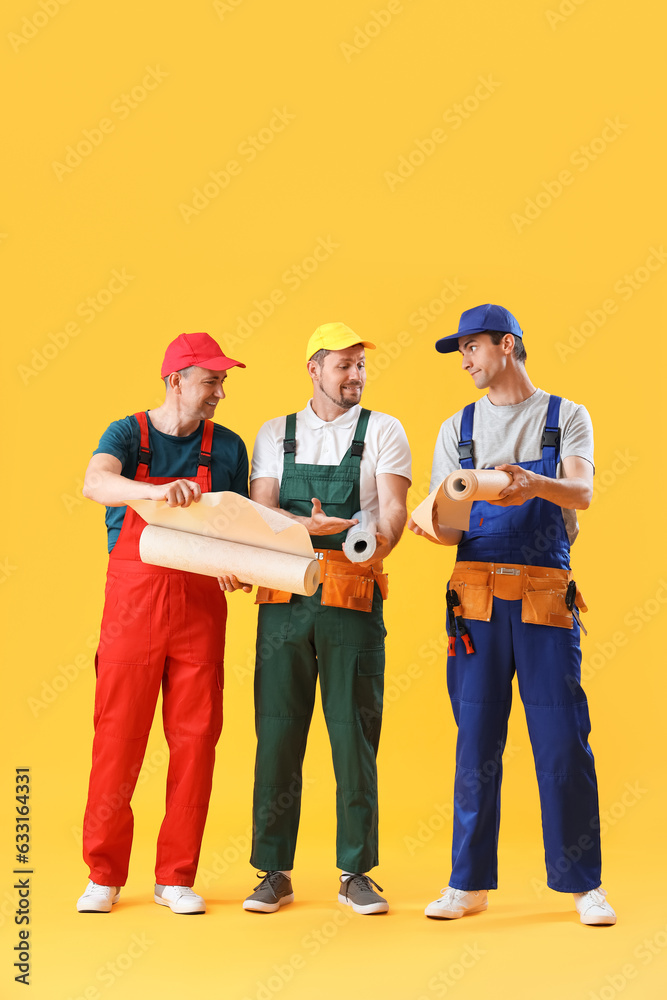 Team of male builders with wallpapers on yellow background