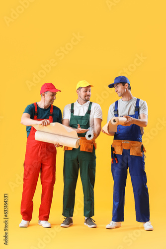 Team of male builders with wallpapers on yellow background © Pixel-Shot