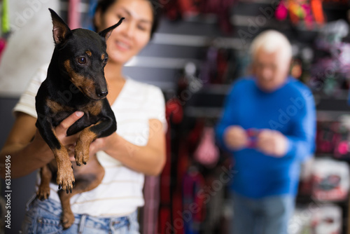 Oriental woman with her little zwergpinscher standing in pet shop. Old man shopping in background. © JackF