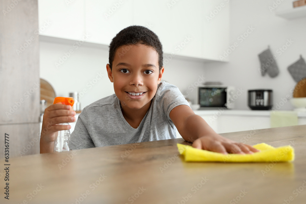 Cute little African-American boy cleaning table with rag in kitchen Cute little African-American boy cleaning table with rag in kitchen