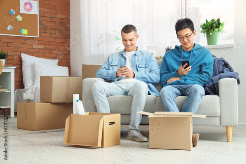 Male students using mobile phones in dorm room on moving day