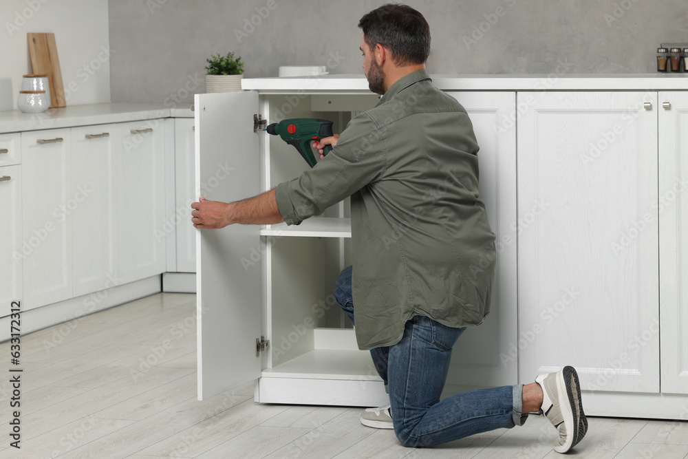 Man with electric screwdriver assembling furniture in kitchen