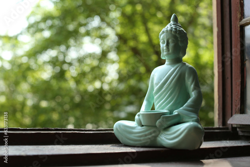 Decorative Buddha statue on wooden windowsill  space for text