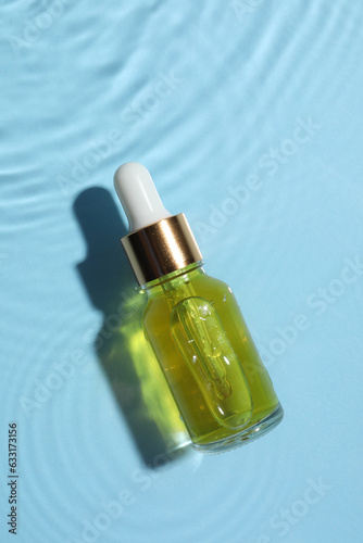 Bottle of cosmetic oil in water on light blue background, top view