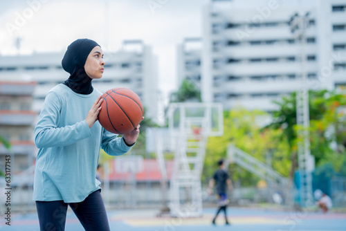 Young asian muslim girl teen wearing hijab going to play basketball on the outdoor court in the morning with determination, Muslim sport concept.