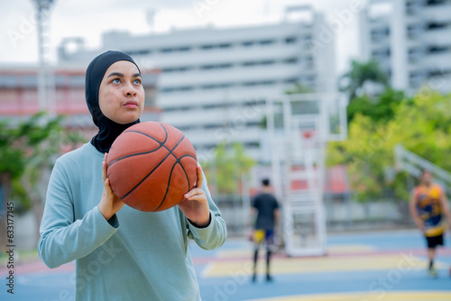 Young asian muslim girl teen wearing hijab going to play basketball on the outdoor court in the morning with determination, Muslim sport concept.