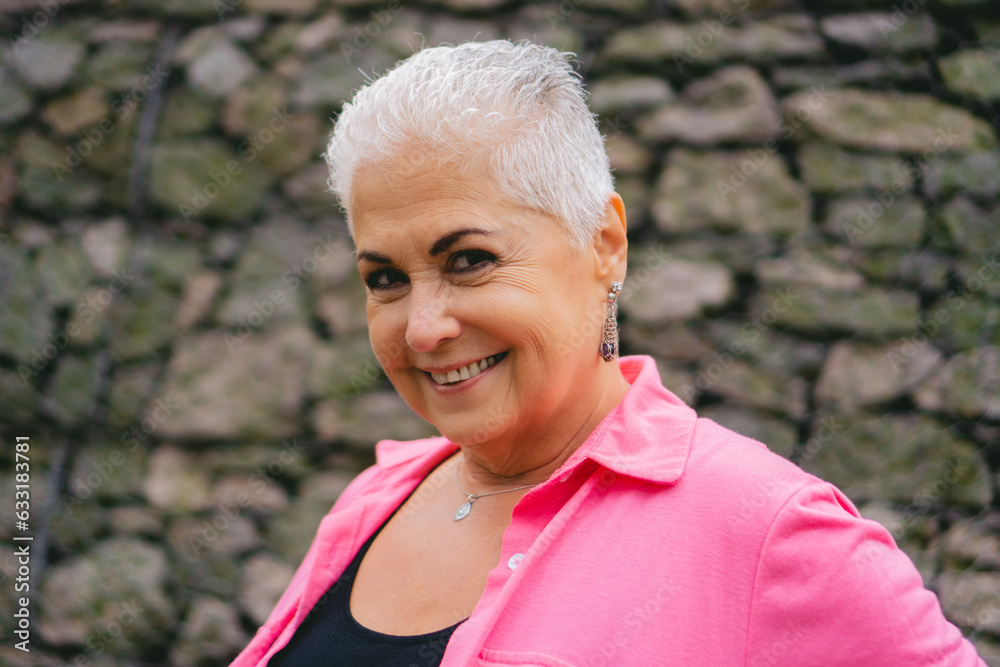 older Latin woman with white hair, look at happy camera, background of stones