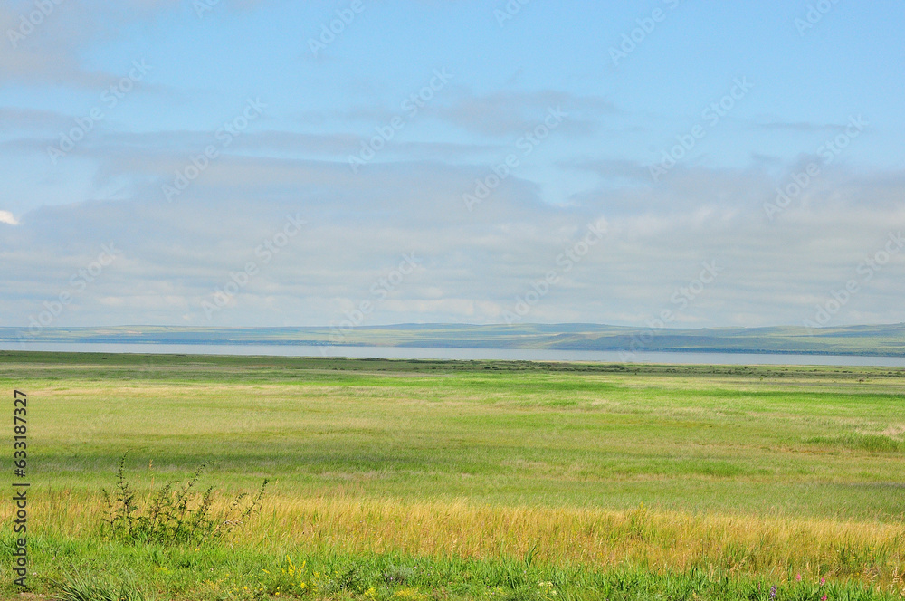 Endless steppe with a range of hills on the shore of a wide lake under a summer cloudy sky.