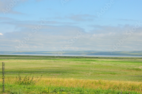 Endless steppe with a range of hills on the shore of a wide lake under a summer cloudy sky.