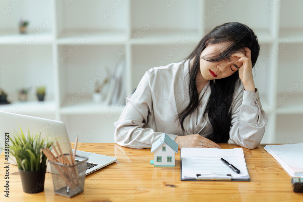 Tired house broker in stress works at a laptop while sitting at a table and holds her hand on her temples, migraine attack.