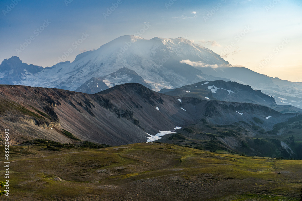 Mount Rainier, Washington in the golden hour with grassy meadow and rocky foothills in the foreground