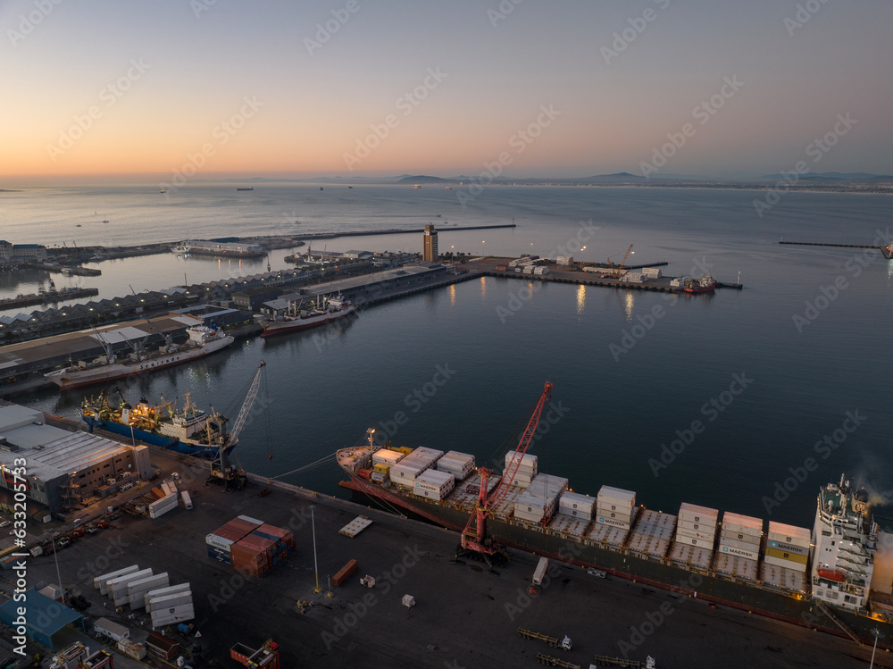 Fototapeta premium Dusk view of the Cape Town commercial port and container ships waiting to complete loading and departure to overseas markets.