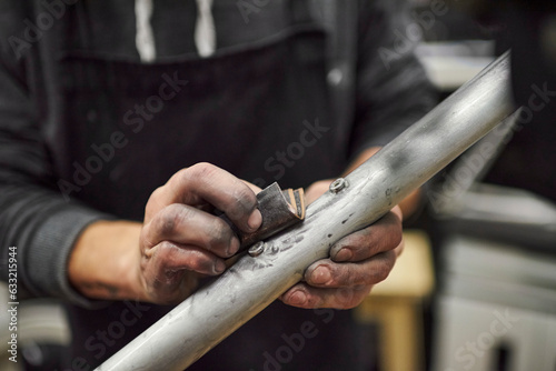 Hands of an unrecognizable person sanding an unpainted bicycle frame as part of the process of a bike renovation work made at his workshop. Close up composition.