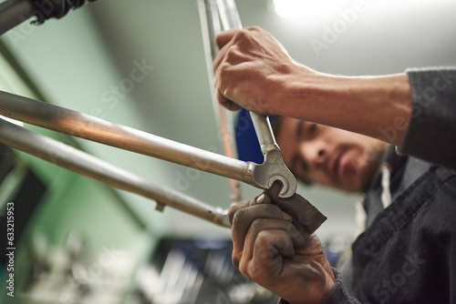 Latin man sanding an unpainted bicycle frame as part of the process of a bike renovation work made at his workshop. Composition with selective focus on the hands.