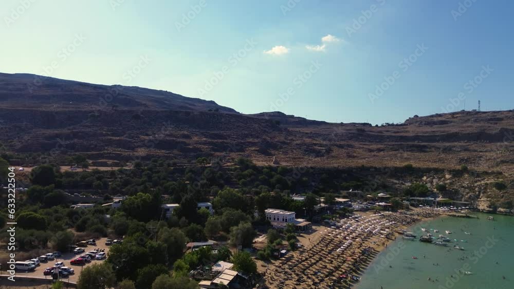 Lindos beach and village in Rhodes, Greece with Acropolis of Lindos, houses and Mediterranean sea during the day filmed with the drone Lindos beach and village in Rhodes, Greece with Acropolis of Lindos, houses and Mediterranean sea during the day filmed with the drone
