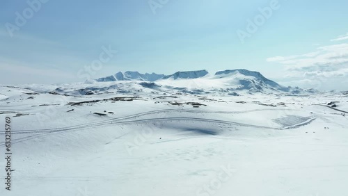 Hurrungane and Jotunheimen mountains seen from top of road crossing mountain Sognefjellet in Norway - Snowmobile tracks crossing snow in foreground photo