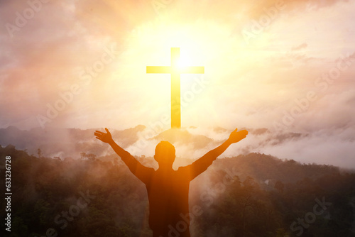 man raising his arms on the mountain cross and light