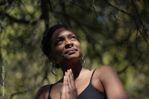 Fotografie, Obraz A nonbinary person presses their palms together in a prayerful pose, and looks up towards the sunlight