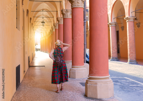 Young female tourist dressed casually standing with hat in the famous arched galleries in Bologna city in Italy. Bologna is student city and home to the oldest university in the world photo
