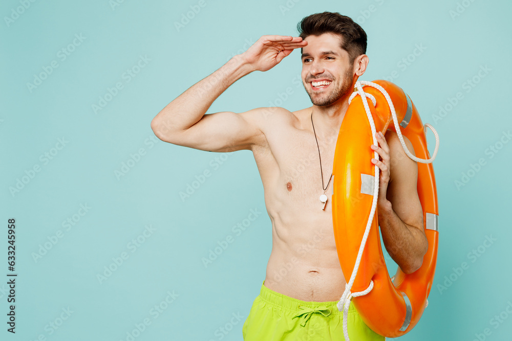 Young man wear green shorts swimsuit whitsle relax near hotel pool hold in hand lifebuoy look far away distance isolated on plain light blue cyan background. Summer vacation sea rest sun tan concept.