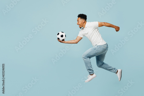 Fototapeta Naklejka Na Ścianę i Meble -  Full body side profile view happy young man fan wear t-shirt cheer up support football sport team jump high hold catch soccer ball watch tv live stream isolated on plain pastel blue color background.