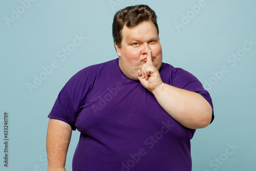 Young secret chubby overweight fat man wearing purple t-shirt casual clothes say hush be quiet with finger on lips shhh gesture isolated on plain pastel light blue cyan background. Lifestyle concept. photo