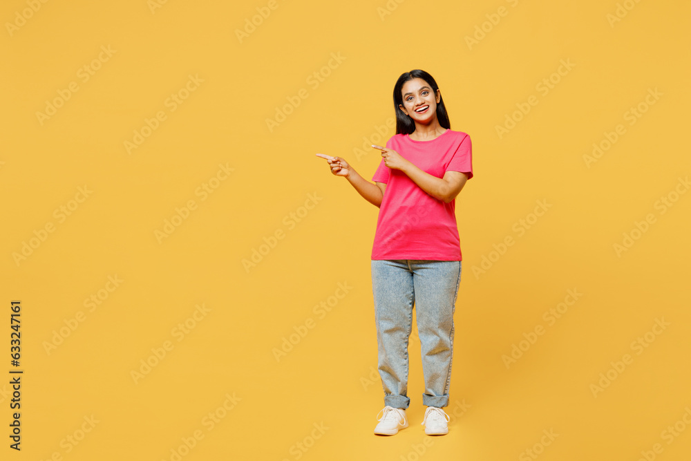 Full body young happy Indian woman wearing pink t-shirt casual clothes point indicate on workspace area copy space mock up isolated on plain yellow wall background studio portrait. Lifestyle concept. Full body young happy Indian woman wearing pink t-shirt casual clothes point indicate on workspace area copy space mock up isolated on plain yellow wall background studio portrait. Lifestyle concept.