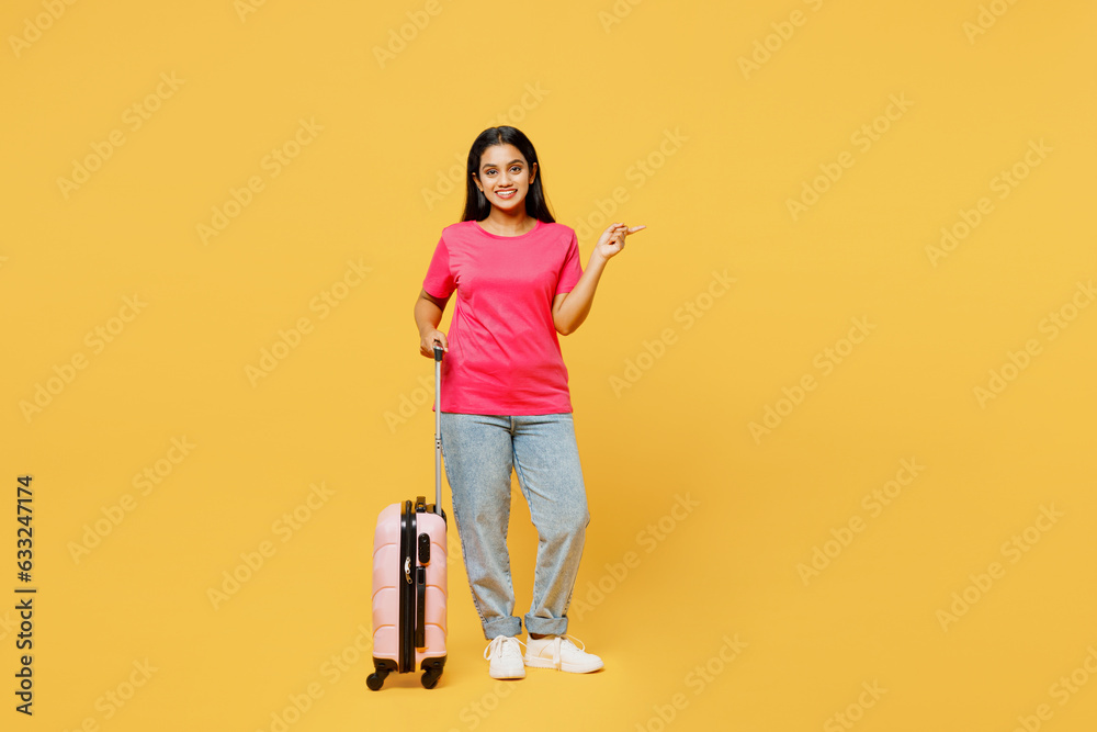 Traveler fun Indian woman wearing casual clothes hold suitcase point aside isolated on plain yellow background. Tourist travel abroad in free spare time rest getaway. Air flight trip journey concept. Traveler fun Indian woman wearing casual clothes hold suitcase point aside isolated on plain yellow background. Tourist travel abroad in free spare time rest getaway. Air flight trip journey concept.