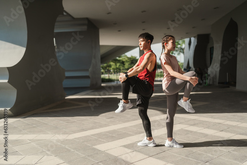 Young Asian couple stretching together before jogging exercise in urban area. Warming up for workout outdoor in the morning.
