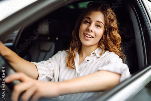 Beautiful smiling woman driving a car. The driver is a woman driving. Summer outdoor portrait. Car travel, lifestyle concept. © maxbelchenko