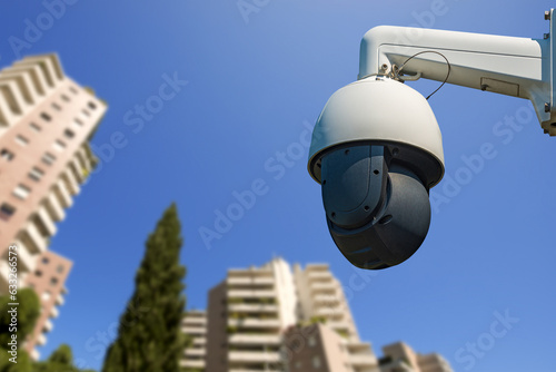 Closeup of a modern security camera against a clear blue sky with blurred skyscrapers on background. photo