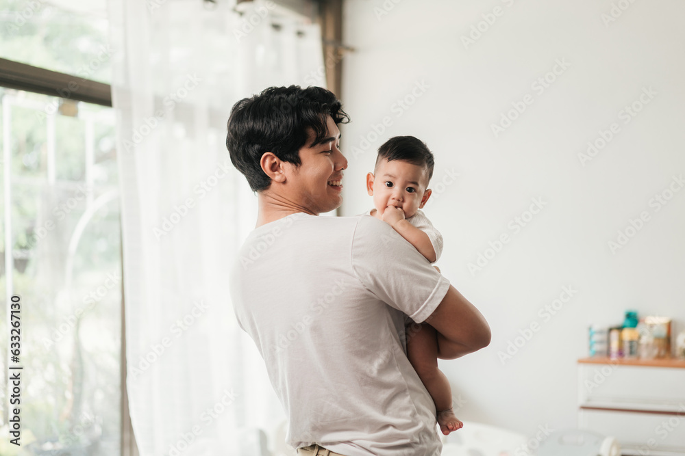 Happiness of fatherhood. Young Asian dad with adorable baby on his hands standing near window at home. Loving father spending time with infant child. Fathers day concept. Happiness of fatherhood. Young Asian dad with adorable baby on his hands standing near window at home. Loving father spending time with infant child. Fathers day concept.
