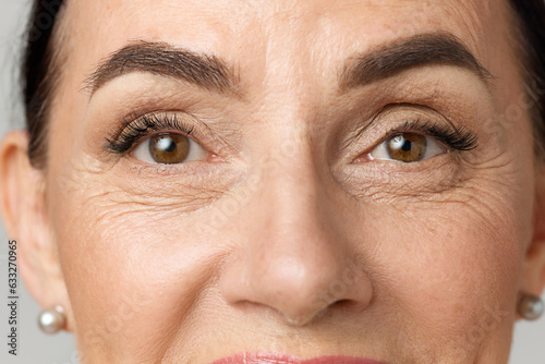 Leinwand Poster Closeup portrait of middle aged woman face with brown eyes over grey background