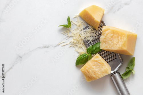 Parmesan cheese with basil leaves and iron grater on marble table top view, cooking background photo