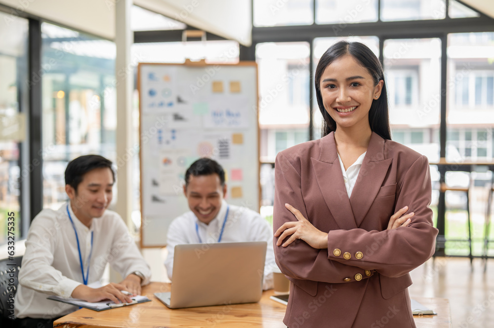 A confident Asian businesswoman stands with her arms crossed in a meeting room A confident Asian businesswoman stands with her arms crossed in a meeting room