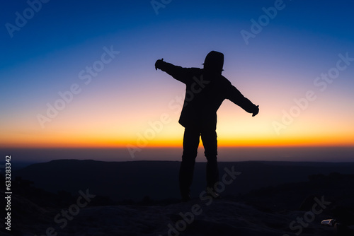 silhouette of a person standing on a mountains at sunrise