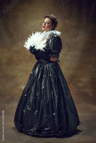 Full lenght portrait of woman in ball dress made of garbage bags and fan in hand in vintage room. Portrait of aristocratic women.