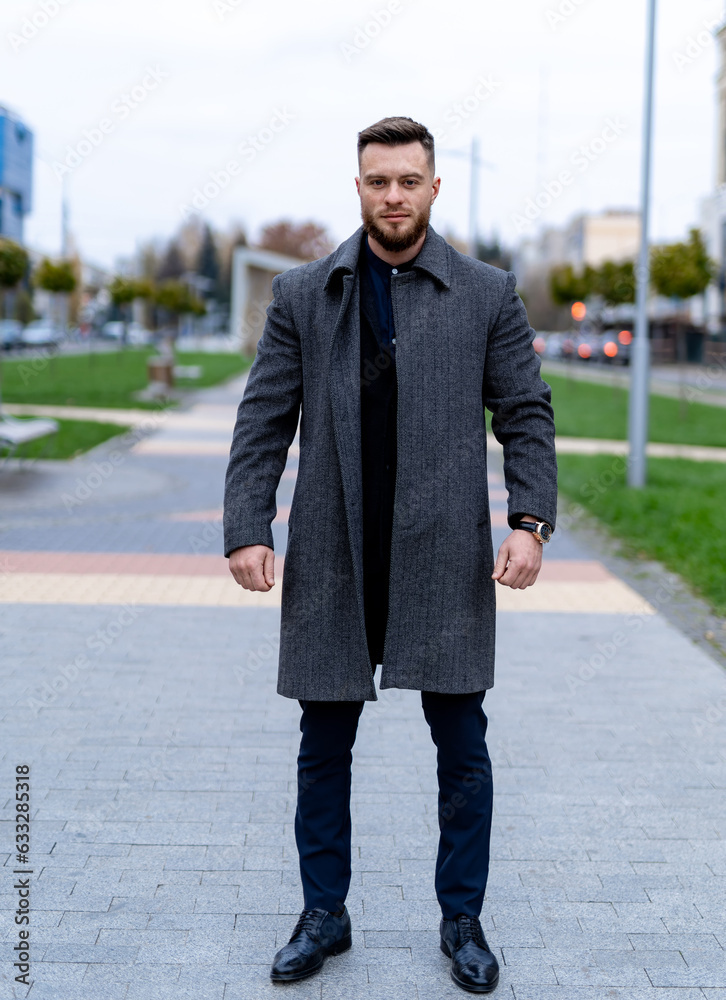 Sstylish man in a coat standing on a sidewalk. A man standing on a sidewalk wearing a coat Sstylish man in a coat standing on a sidewalk. A man standing on a sidewalk wearing a coat