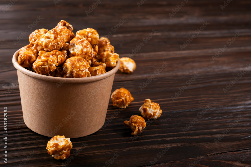 Caramelized popcorn in paper bucket on wooden kitchen table