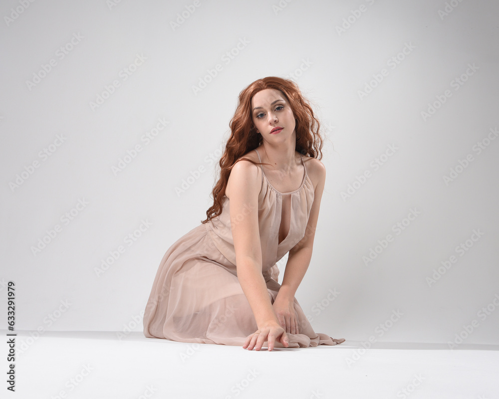 Full length portrait of beautiful brunette model wearing a pink dress. graceful sitting pose, kneeling on floor gestural hands. shot from low angle perspective, isolated on white studio background Full length portrait of beautiful brunette model wearing a pink dress. graceful sitting pose, kneeling on floor gestural hands. shot from low angle perspective, isolated on white studio background