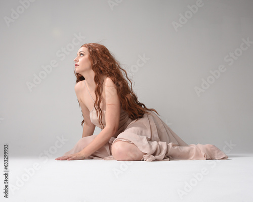 Full length portrait of beautiful brunette model  wearing a  pink dress. graceful sitting  pose  kneeling on floor gestural hands. shot from low angle perspective   isolated on white studio background